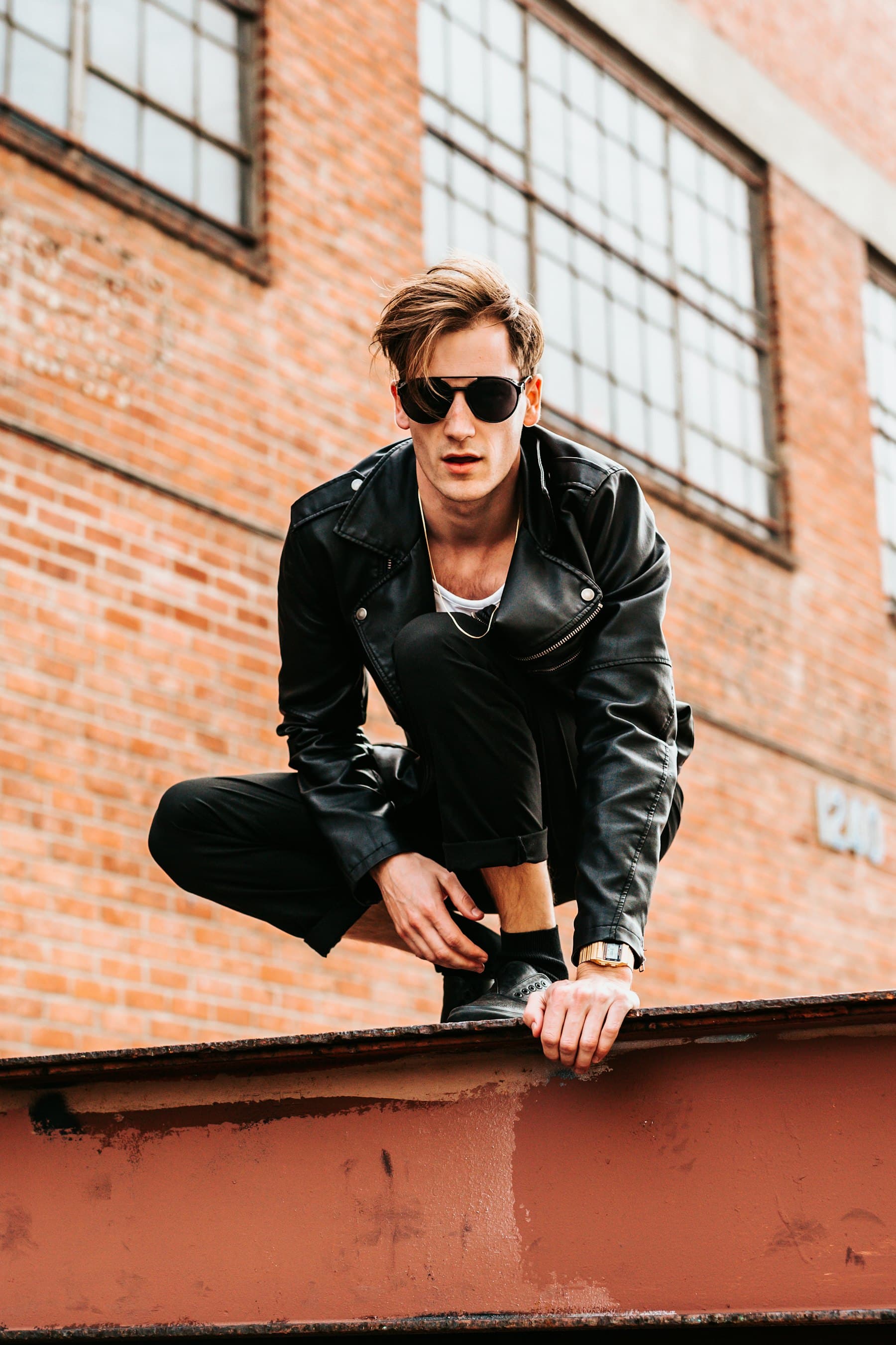 Model in a leather jacket crouched on a rooftop ledge